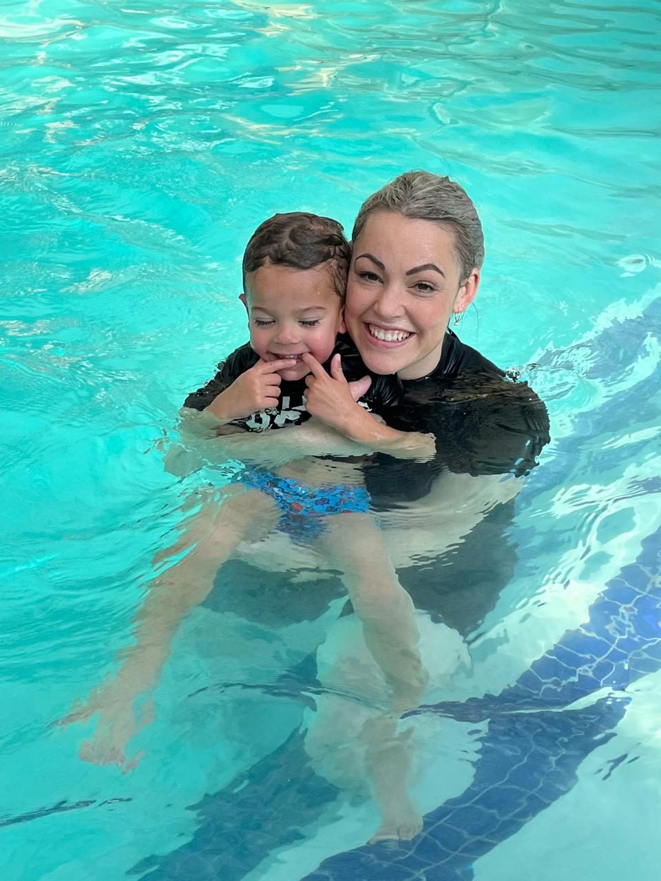 An instructor holding a smiling toddler in the pool